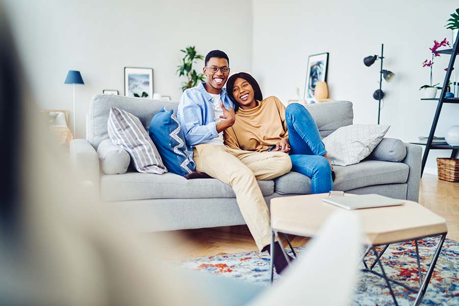 Personal Insurance - Happy Couple Resting Together and Sitting on the Sofa in the Spacious Living Room of Their Modern Apartment